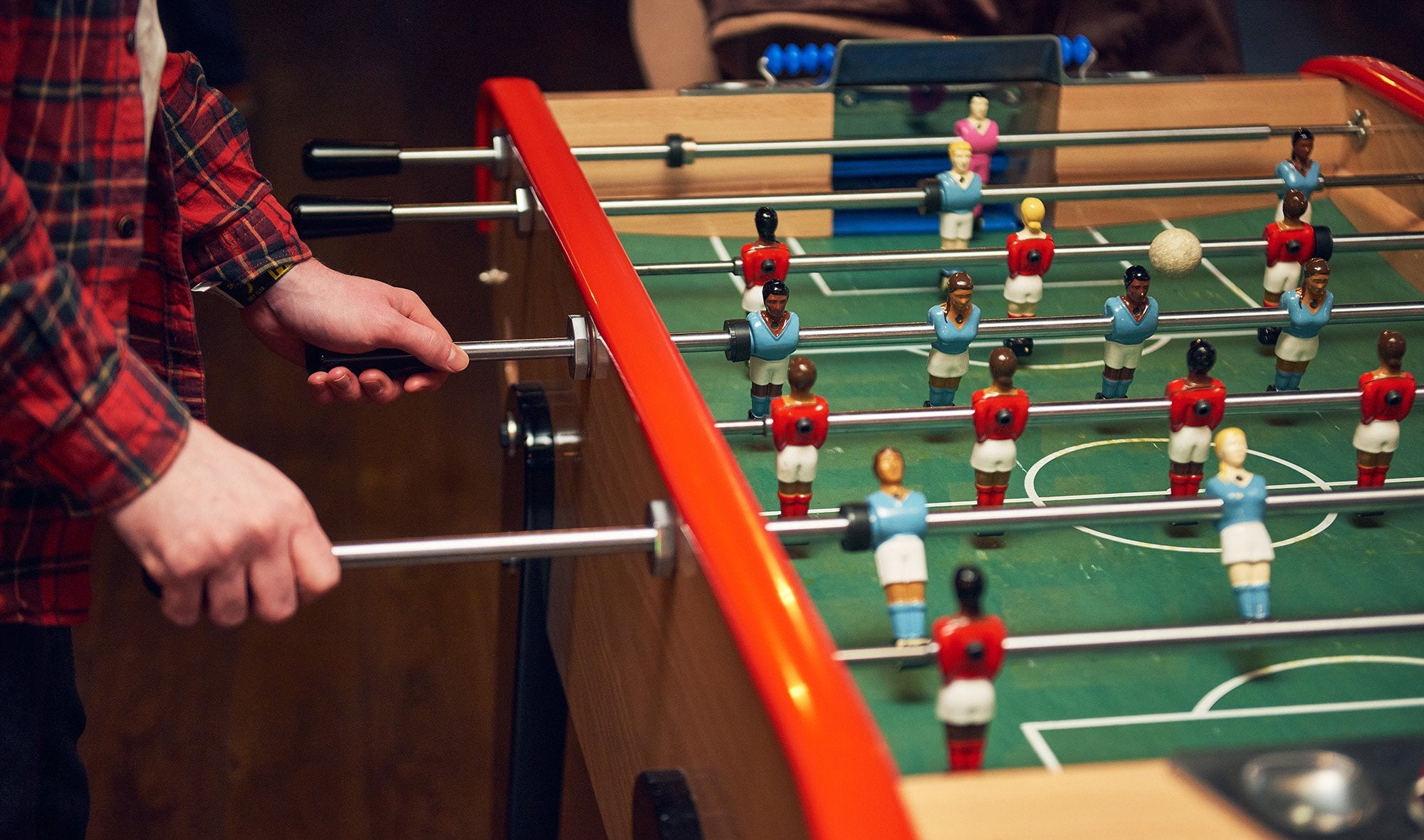 Two people stand on one side of a foosball table, each holding two rods for the black team against the red team.